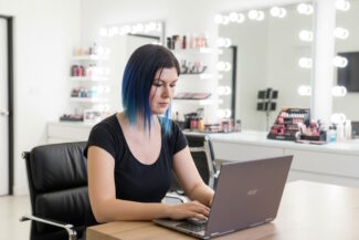Arizona mobile makeup artist managing makeup appointments on a laptop in a professional beauty studio.